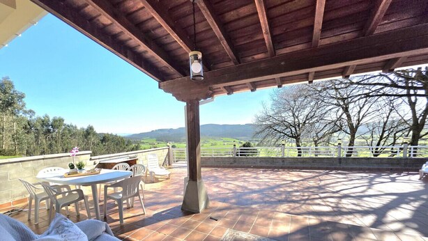 An outdoor patio with a wooden pergola, a table with chairs, and a view of the countryside. - La Encina de Güemes - 13008 (Güemes)