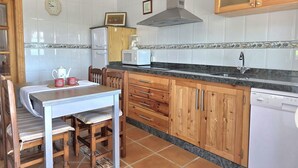 A kitchen with wooden cabinets, a white dishwasher, a coffee maker, and a clock on the wall. - La Encina de Güemes - 13008 (Güemes)