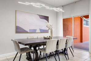 Un espace de salle à manger moderne, avec une grande table, des chaises, un vase de fleurs et un luminaire contemporain.