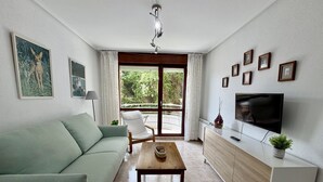 A living room with a sofa, a wooden coffee table, a TV, and a balcony with curtains. - Apartment Playa Azul - 5924 (Isla)