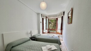 A room with two beds, a window with curtains, a lamp, and a hanging light fixture. - Apartment Playa Azul - 5924 (Isla)