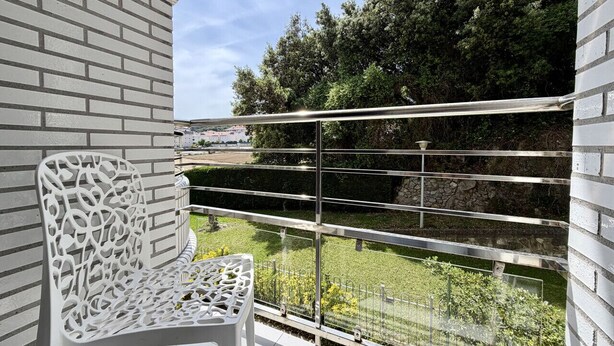 A balcony with a white chair, metal railing, and a view of greenery and trees. - Apartment Playa Azul - 5924 (Isla)