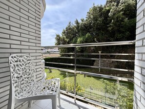 A balcony with a white chair, metal railing, and a view of greenery and trees. - Azul Beach Apartment - 5924 (Isla)