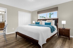 Un dormitorio con cama de madera, una mesita de noche, una silla y una ventana con vista a palmeras.