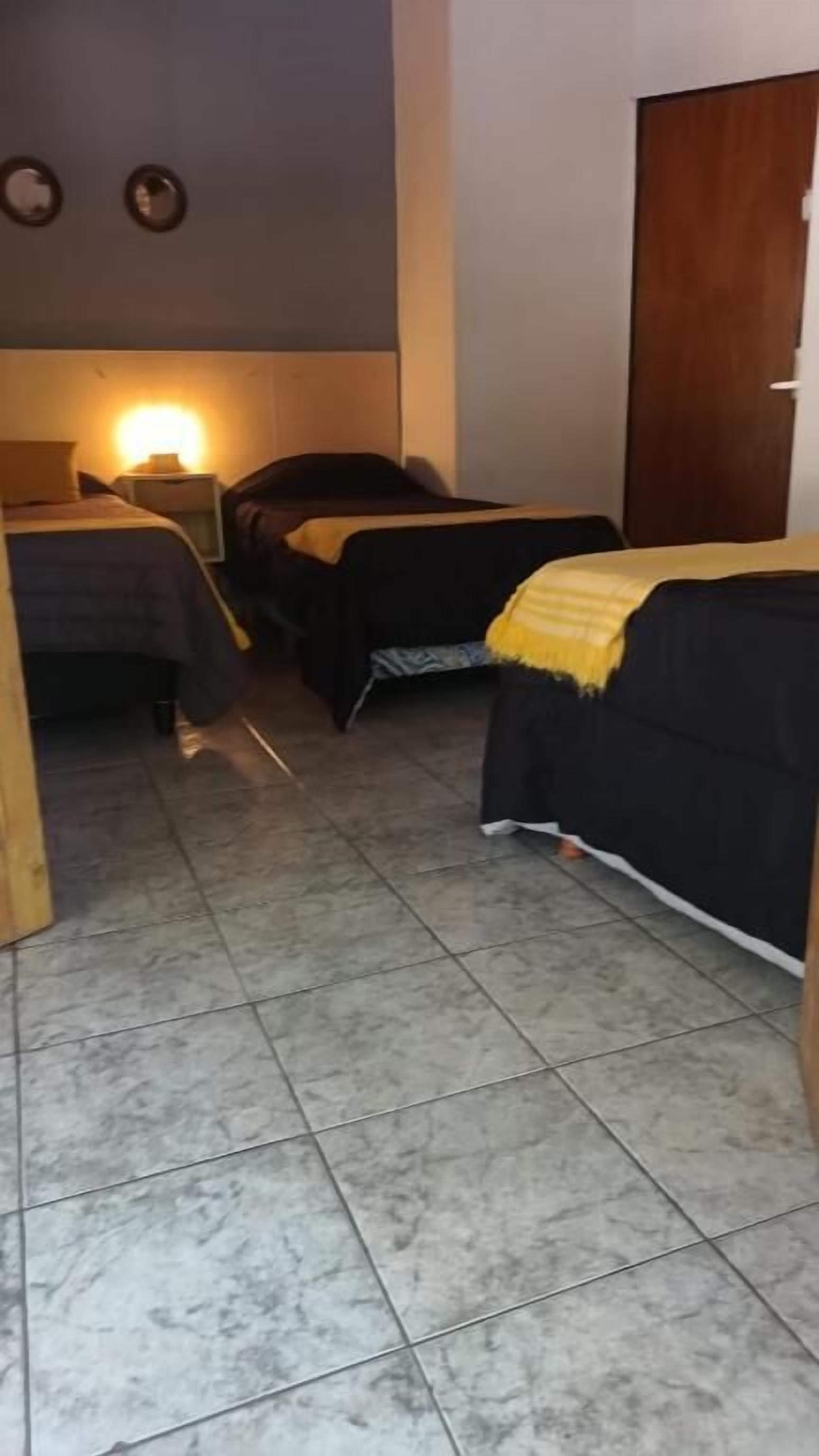 Camera d'albergo con due letti, un armadio in legno, pavimento piastrellato e una lampada fissata al muro.