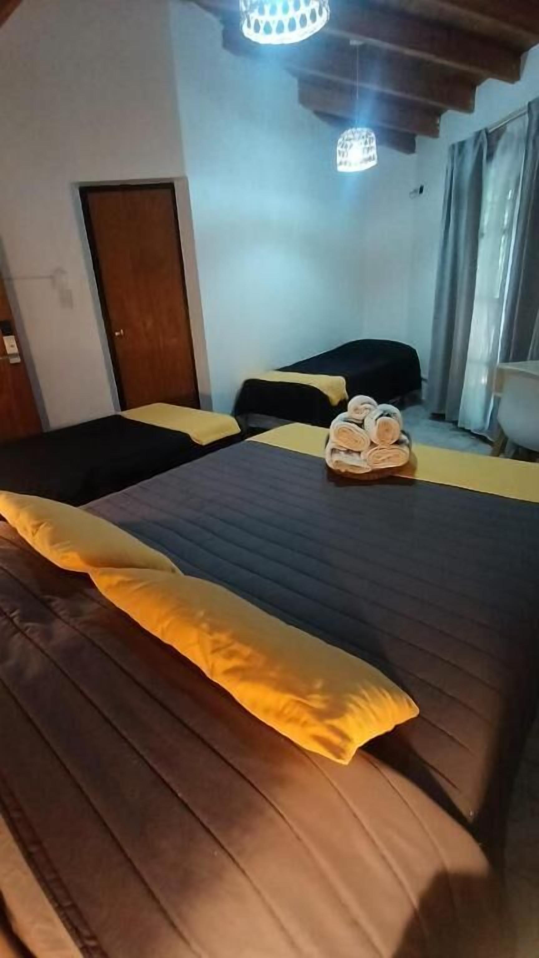 Una cama bien tendida con una colcha oscura y una sola almohada amarilla.