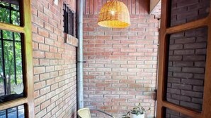 A small, enclosed patio area with a brick wall, a wicker chair, a small round table with a potted plant, and a hanging light fixture. - Hotel Alta Mendoza (Mendoza)