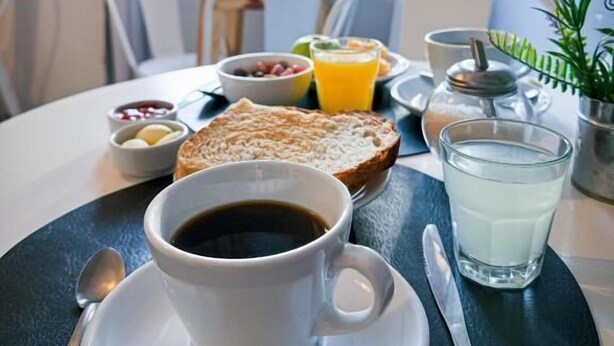 A breakfast setting with a cup of coffee, toast, fruit, and a glass of milk on a table. - Hotel Alta Mendoza (Mendoza)