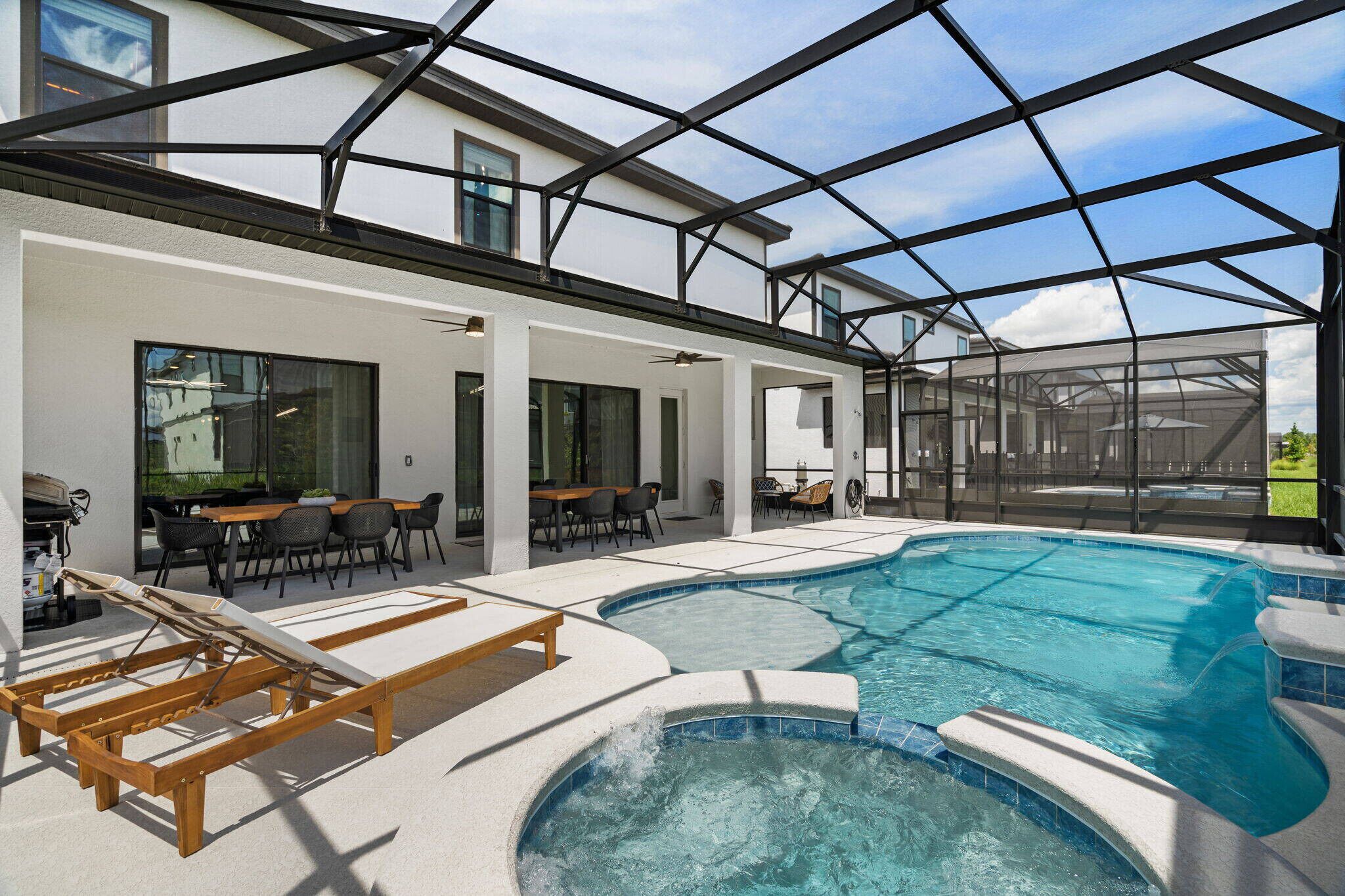 Ein Swimmingpool mit Liegestuhl, einer überdachten Terrasse und Blick auf ein Haus.