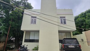 A two-story building with a flat roof, a central pillar, and a parked car and motorcycle in front. - R J Residency  (Varanasi)