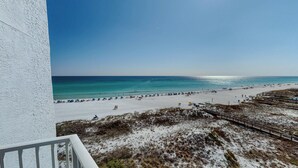 Vista da praia com um prédio branco, areal e céu azul límpido.