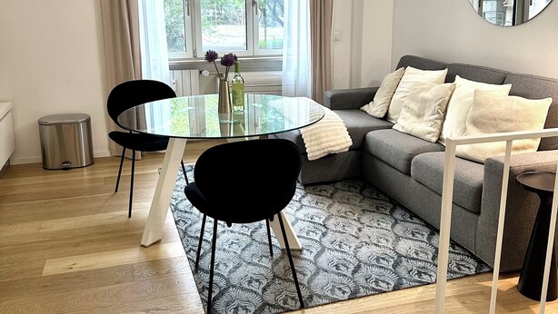 A modern living room with a grey sofa, a round mirror, a glass dining table with chairs, and a patterned rug. - Boutique Apartment 60sqm between Sempione & CityLife with Studio Space (Milano)