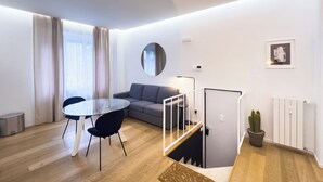 A modern living room with a round mirror, grey sofa, round dining table with black chairs, and a staircase with a glass railing. - Boutique Apartment 60sqm between Sempione & CityLife with Studio Space (Milano)