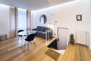 A modern living room with a round mirror, grey sofa, round dining table with black chairs, and a staircase with a glass railing. - Boutique Apartment 60sqm between Sempione & CityLife with Studio Space (Milano)
