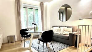 A modern living room with a sofa, a dining table with chairs, a large window, and a mirror on the wall. - Boutique Apartment 60sqm between Sempione & CityLife with Studio Space (Milano)