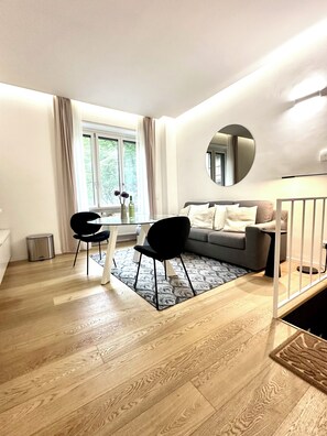 A modern living room with a sofa, a dining table with chairs, a large window, and a mirror on the wall. - Boutique Apartment 60sqm between Sempione & CityLife with Studio Space (Milano)