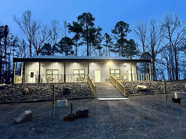 A two-story building with a staircase leading to the entrance, surrounded by trees and gravel.