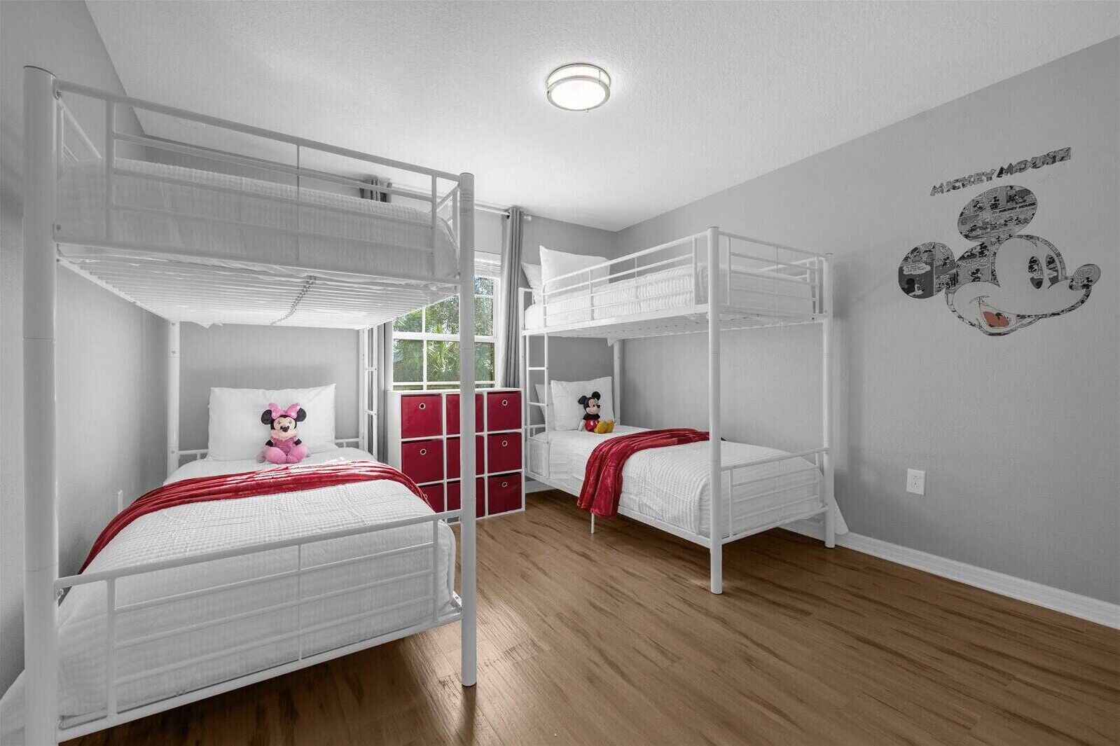 A room with bunk beds, a Mickey Mouse wall decal, and a window with a view.