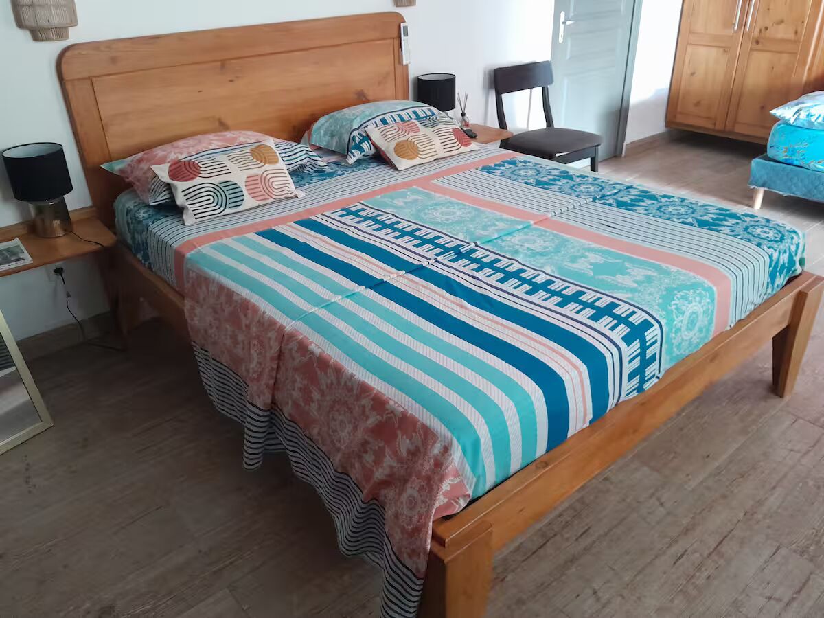 Un lit en bois avec une couvre-lit à rayures, une table de chevet avec une lampe et une chaise dans une pièce au plancher de bois et dotée d’une armoire.