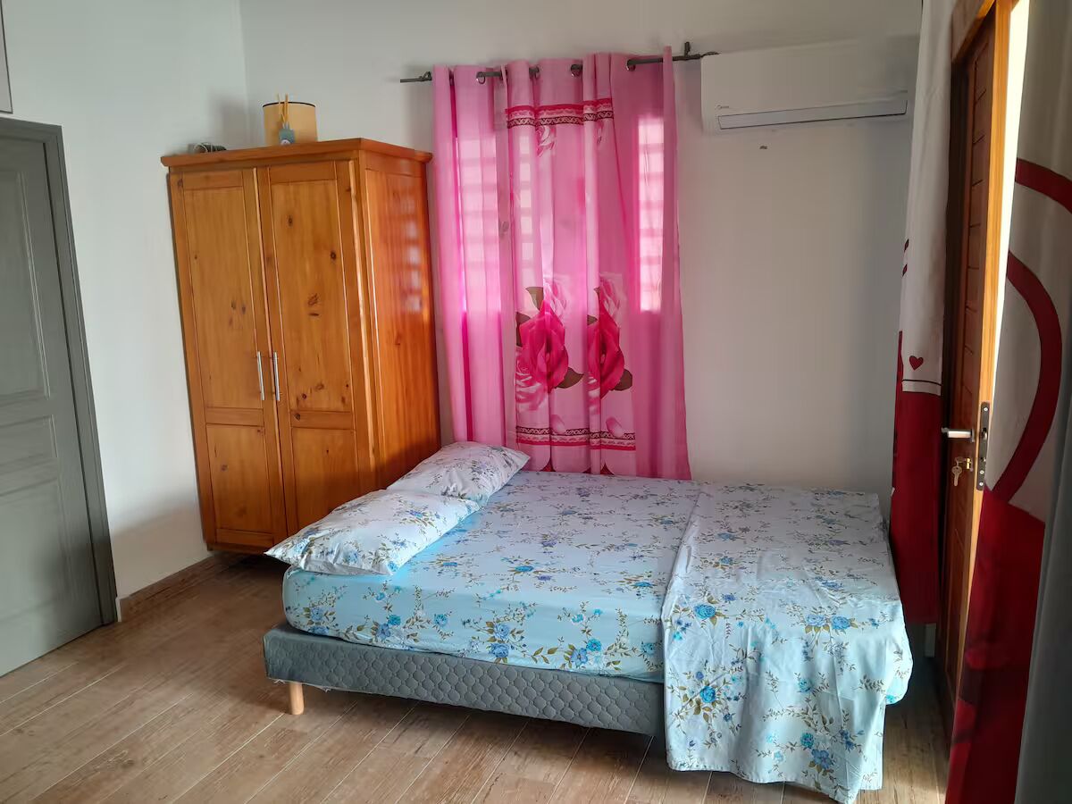 A bedroom with a bed, wooden wardrobe, and pink curtains.