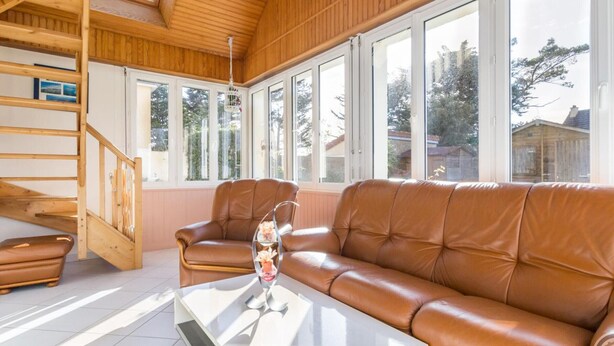 Ein gemütliches Wohnzimmer mit einem braunen Ledersofa, einem Glastisch und einer Holztreppe.