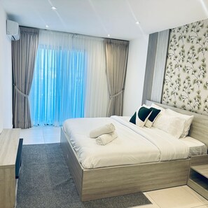 A modern hotel room with a bed, curtains, a headboard with a floral pattern, and a view of the outdoors. - The Pearl in the City  (Accra)