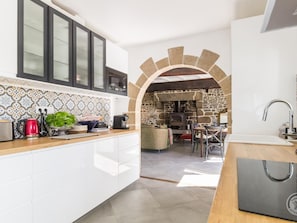 A modern kitchen with white cabinets, a stone archway, a stone fireplace, and a dining area with chairs. - Rustic house with garden - 4 guests (Sourdeval)