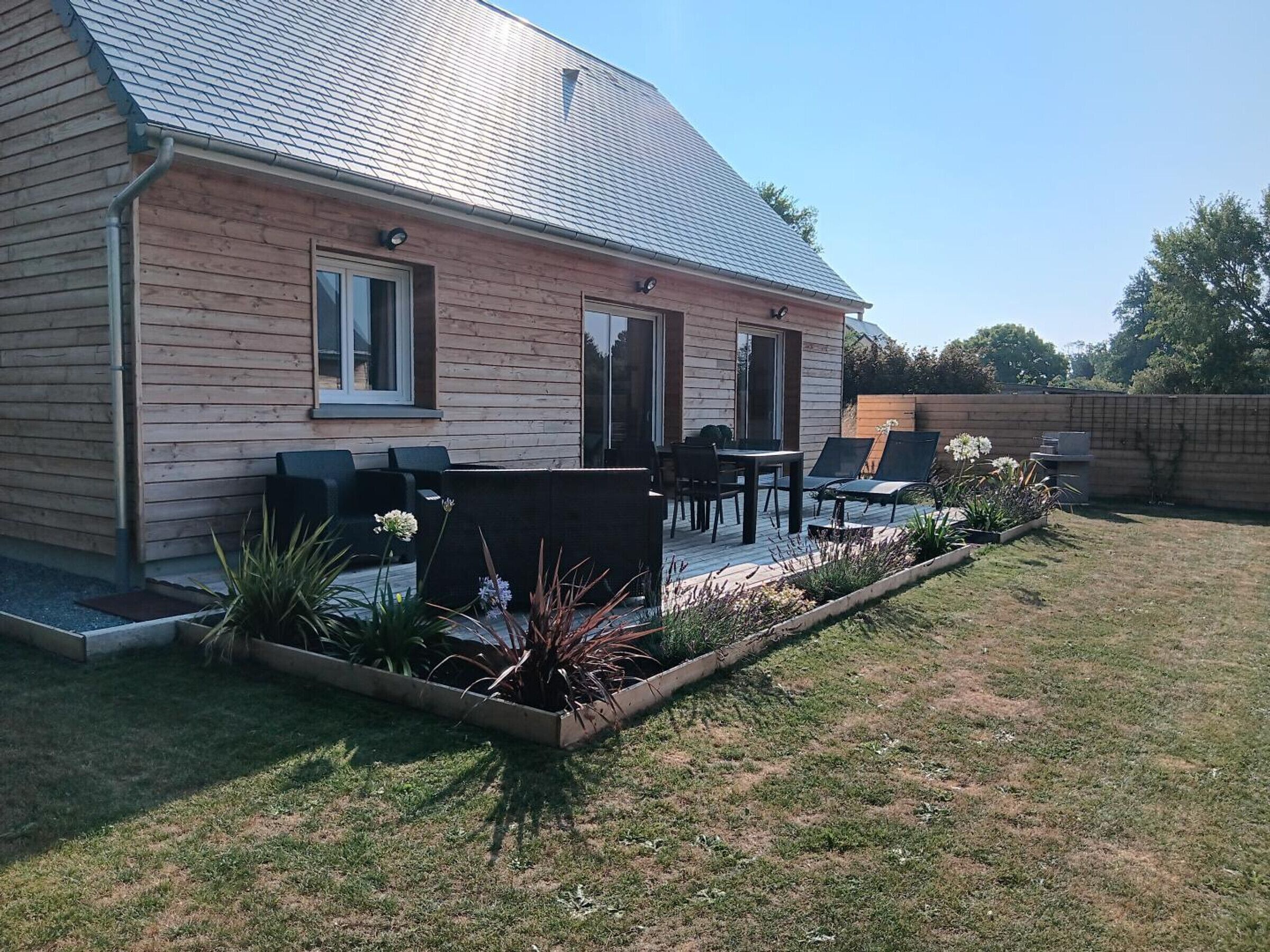 Une maison dotée d’un patio aménagé avec du mobilier d’extérieur et d’un parterre fleuri.