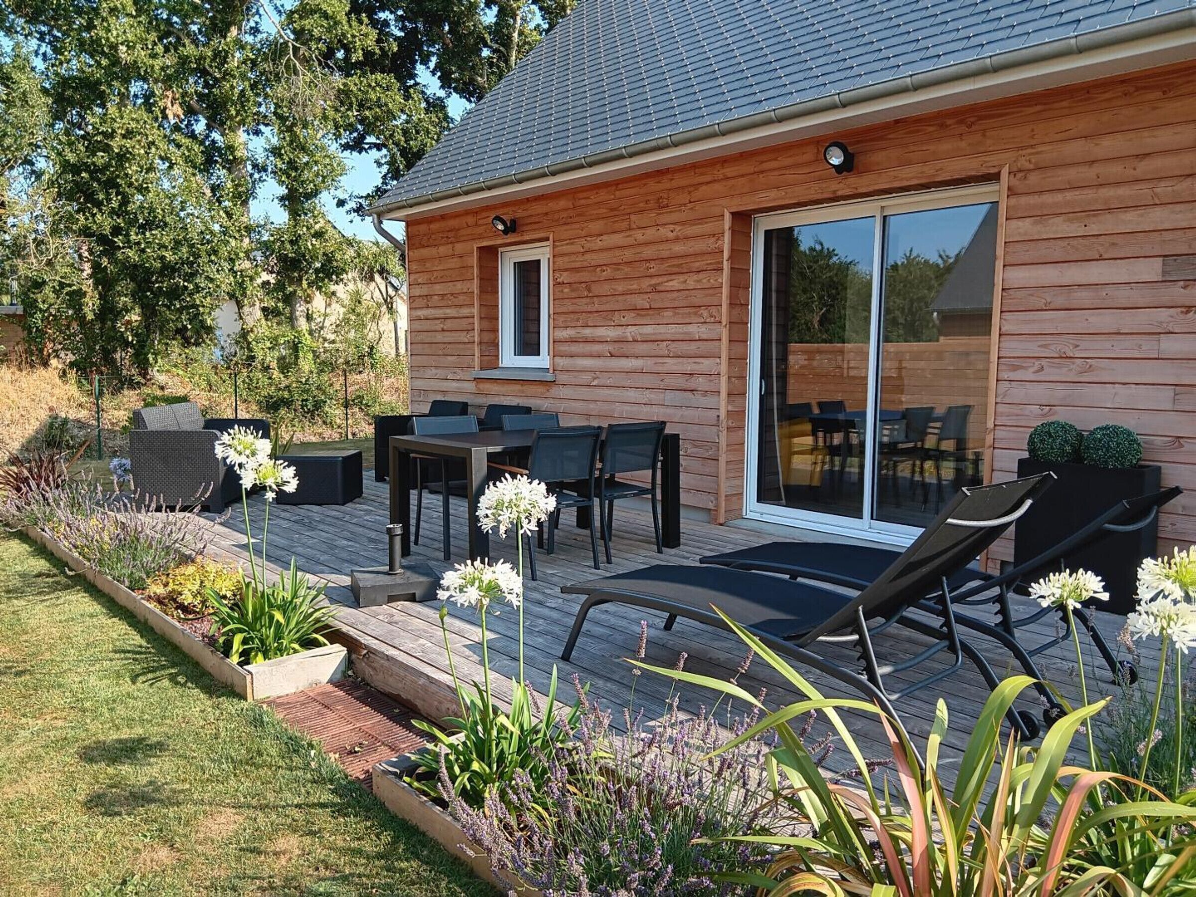 A wooden house with a deck, outdoor furniture, and a garden.