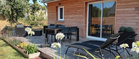 A wooden house with a deck, outdoor furniture, and a garden.