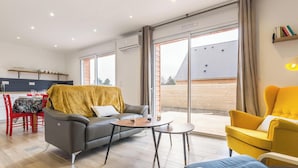 Un salon moderne avec un canapé, un fauteuil jaune et un coin repas comprenant une table et des chaises.