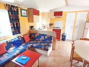 A compact living space with a sofa, a small table, a dining table, and a kitchenette. - Mobile home with AC - 6 guests (Bourg-Charente)
