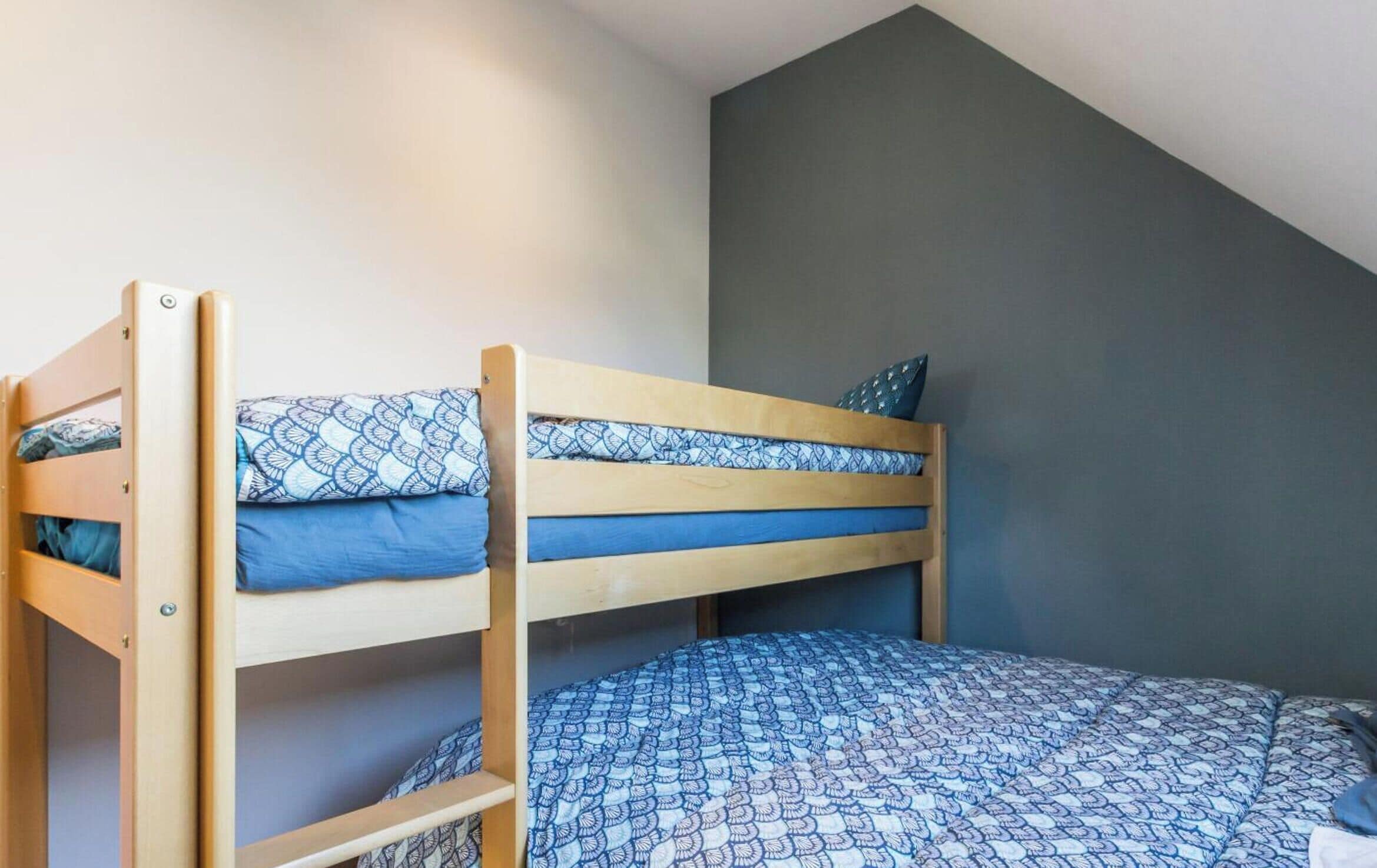 Una cama litera con ropa de cama estampada en una habitación con techo inclinado y pared oscura.