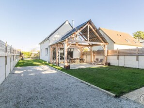 Ein Haus mit überdachter Terrasse, Kiesauffahrt und gepflegtem Rasen.