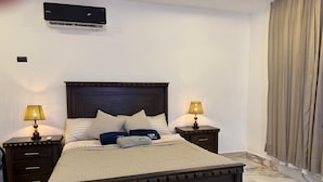 A bedroom with a bed, two bedside tables with lamps, a wall-mounted air conditioner, and a curtain on the window. - Discover a place for vacations, weekend getaways, or a complete escape. (Don Juan)