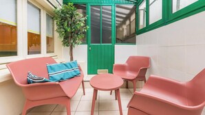 En liten uteplats med två rosa stolar, ett litet runt bord och en grön dörr.