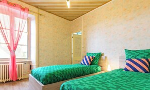 Une chambre avec deux lits, une fenêtre avec un rideau, un radiateur et une porte.