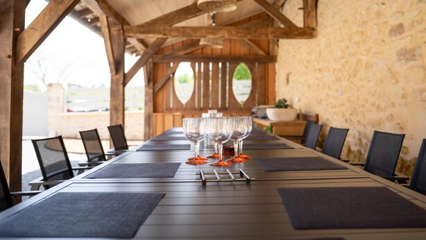 A long dining table with chairs, a hanging light fixture, and a stone wall in the background.