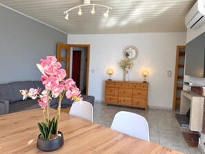 Een eetgedeelte met een houten tafel, stoelen, een potorkidee, een houten kast met twee wandlampen en een televisie op een voetstuk.