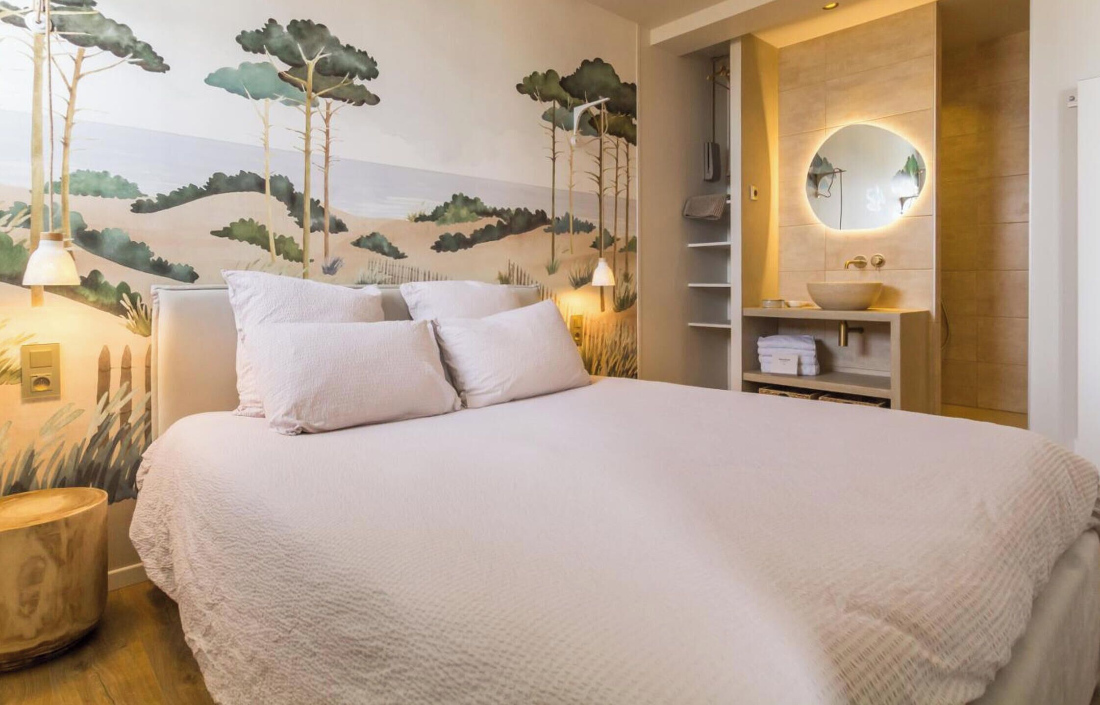 Un dormitorio con una cama, una estantería en la pared, un espejo redondo y un mural con árboles y colinas.