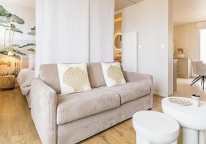 Ein modernes Wohnzimmer mit einem beigefarbenen Sofa, einem weißen Couchtisch und einer großen Pflanze.
