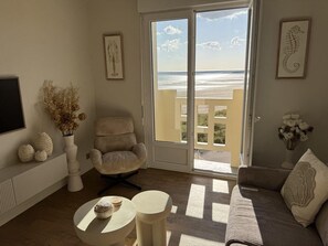 Ein Wohnzimmer mit Blick auf den Strand, ein Sessel, eine Couch, ein kleiner Tisch und Dekorationselemente.