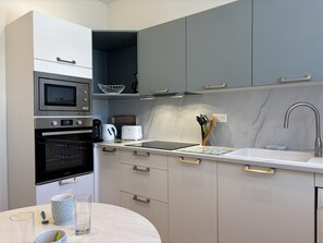 A modern kitchen with built-in appliances, a sink, and a dining area. - Cozy apartment in city centre - 2 guests (Vichy)