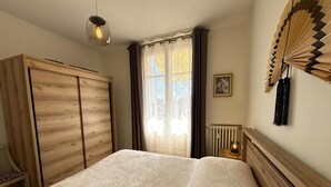 Et soveværelse med en seng, et træskab, en radiator, en loftsvifte og et vindue med gardiner.