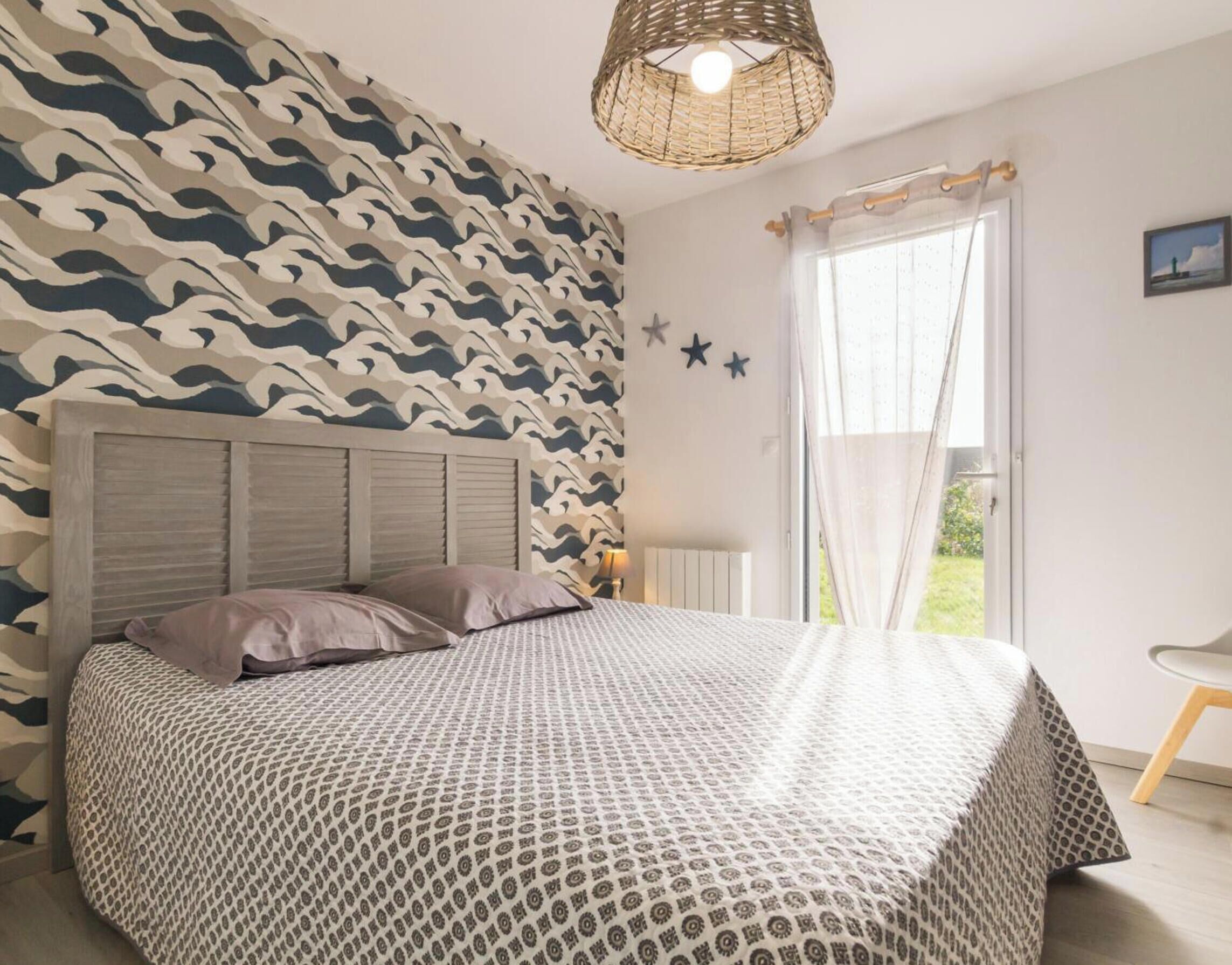 A bedroom with a patterned bedspread, a headboard, a window with curtains, and a star decoration on the wall.