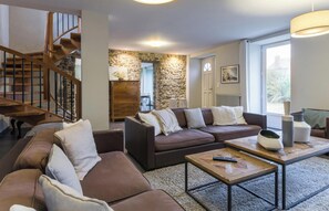 A living room with a brown sofa set, a wooden coffee table, a staircase, and a stone wall. - Detached house with panoramic view - 8 guests (Portbail)