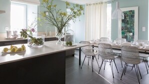 A modern kitchen with a central island, dining area with chairs, and a pendant light. - Detached house with panoramic view - 8 guests (Portbail)