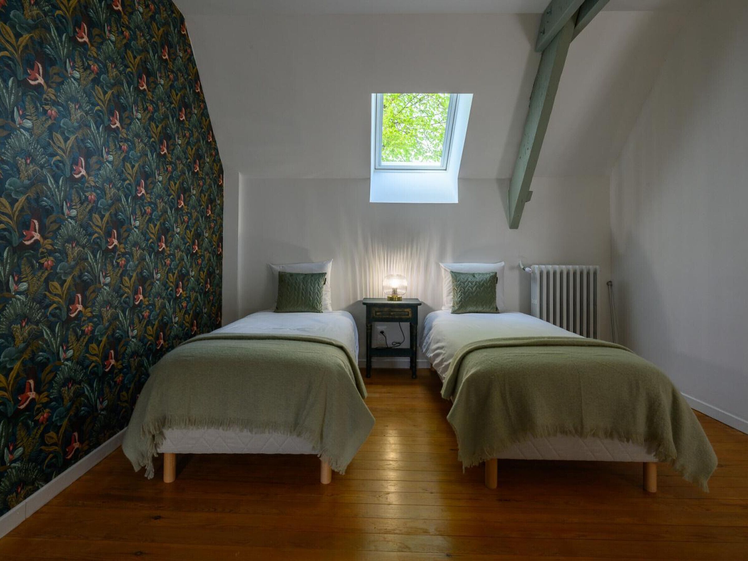 Ein Schlafzimmer mit zwei Betten, einem Fenster, einem Heizkörper und einem Nachttisch.