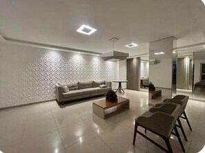 Ein modernes Wohnzimmer mit einer Couch, einem Couchtisch und Sesseln, einer Wand mit Muster und einem Essbereich im Hintergrund.