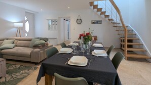 A dining area with a table set for four, a staircase, and a living room with a sofa and a lamp. - House with AC in the heart of the village - 6 guests (SAINT SIMON)